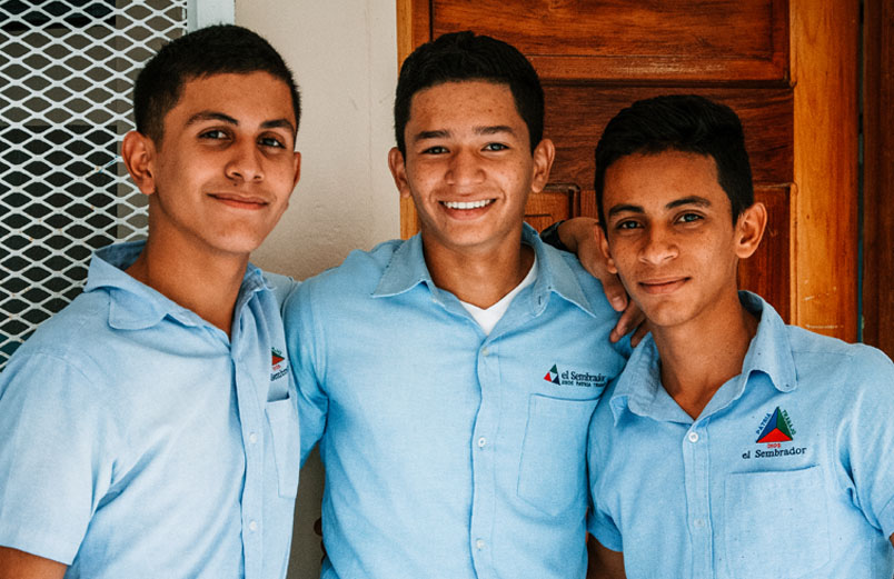 Three smiling students standing inside a building, posing for a photo.