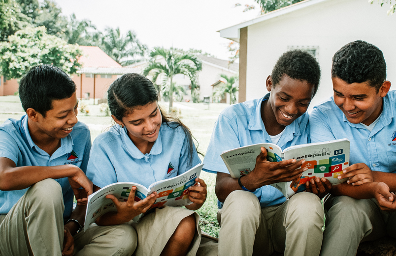 Four students in school uniforms reading and laughing together