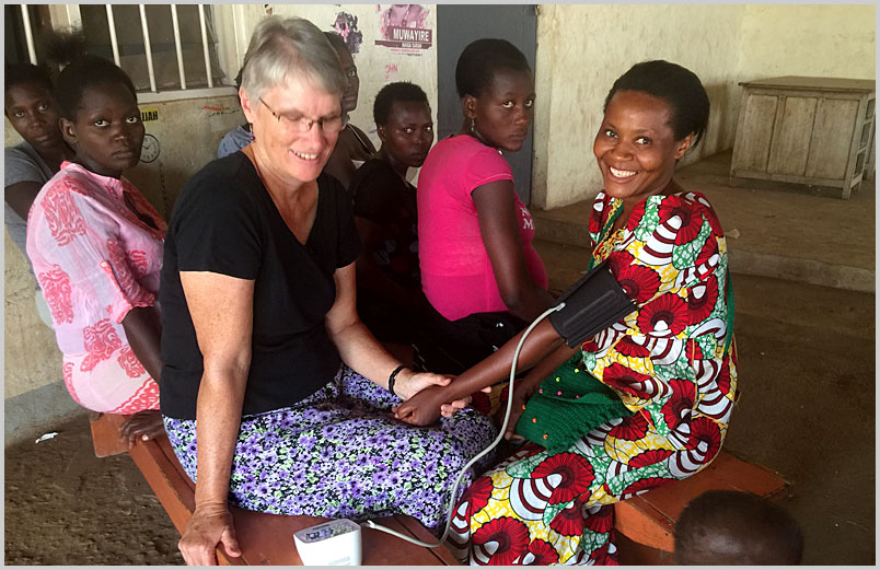 Photo of Christine taking a mother's blood pressure during a prenatal visit in Kampala.