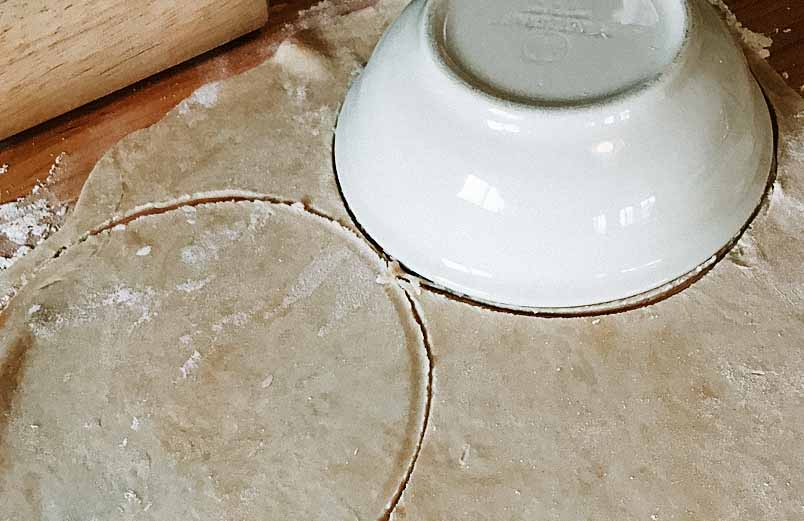 Roll out the dough and cut into large circles. A photo of a cereal bowl being used as a pattern for the circle