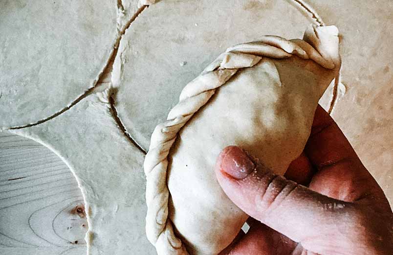 A photo of a hand holding a finished empanada, ready to coat with egg and bake