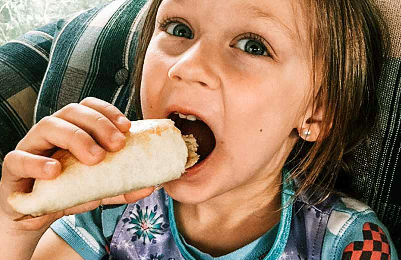 A photo of a young girl taking a big bite of an empanada