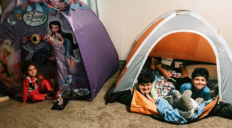 A girl in a Disney princess tent and two boys in a grey and orange tent inside their house