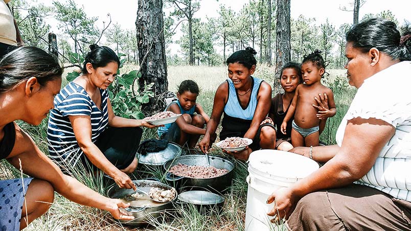 Lilian is still active in ministry and serves as a nurse and the pastor of Casa Sola church in eastern Honduras. A photo of Lillian seated on the ground with several other women preparing plates of food.