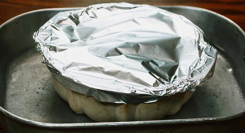 A photo of the bundt pan covered in foil and sitting in a pan of water