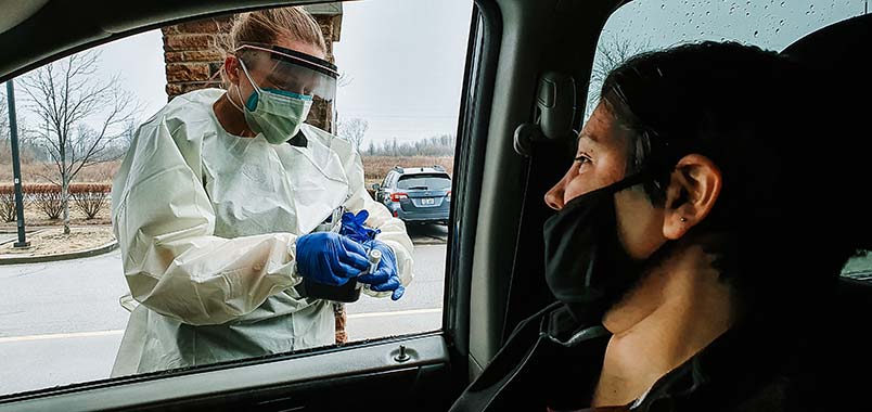 A healthcare worker giving a COVID test to someone in a car