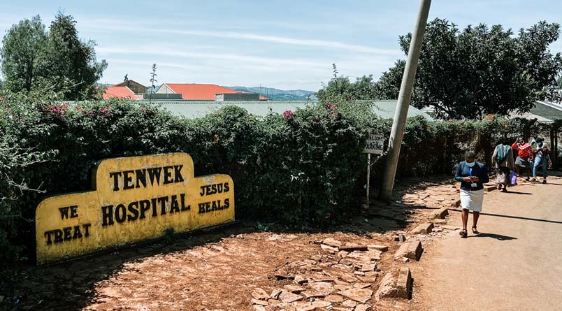 People walking on the road past a sign for Tenwek hopsital.