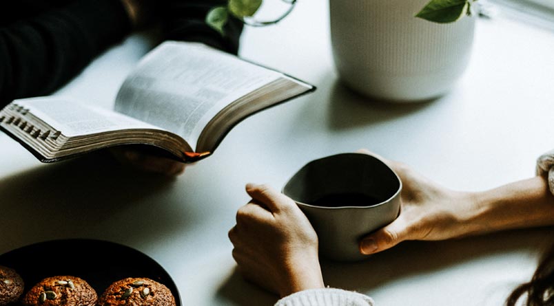 Two people at a table with a Bible, a plate of muffins, and a cup of coffee.