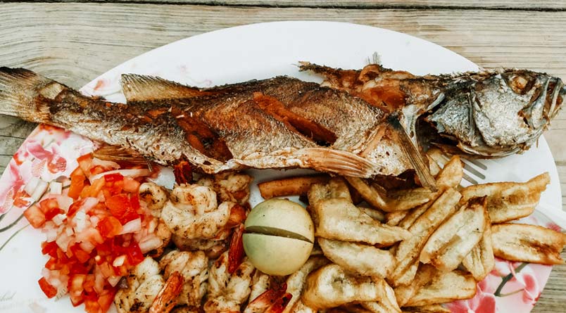 A plate with a cooked whole fish and other delicacies.