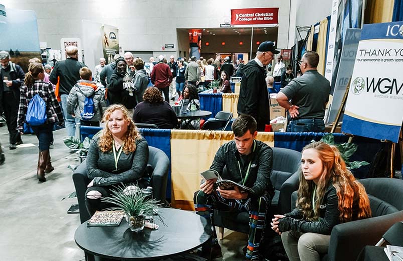 Three people sit in chairs at a conference booth in the exhibit hall.