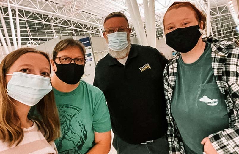 Four adults wearing masks posing for a photo in a large building, possibly an airport.