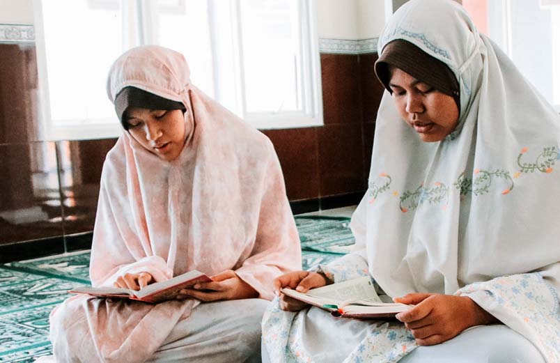 Two women sitting crosslegged on the floor reading