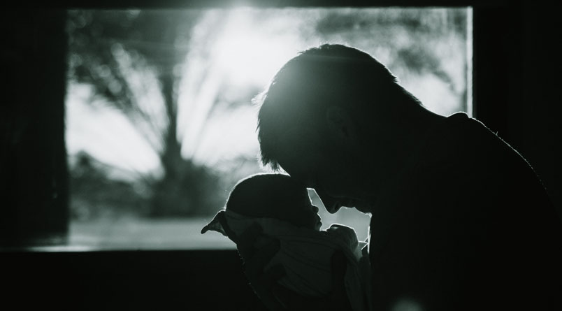 The profile of a man holding an infant in front of a window
