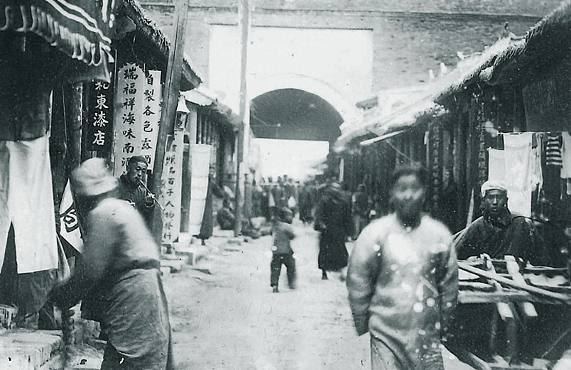 A black and white photo of people walking along a street in China during the early 1900s