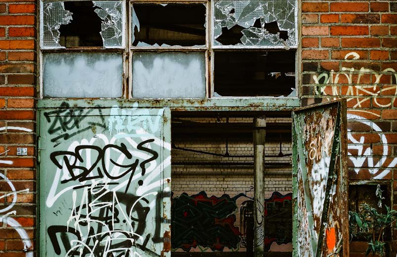 Looking through an open double-door of a warehouse with broken windows, covered with graffiti inside and out.