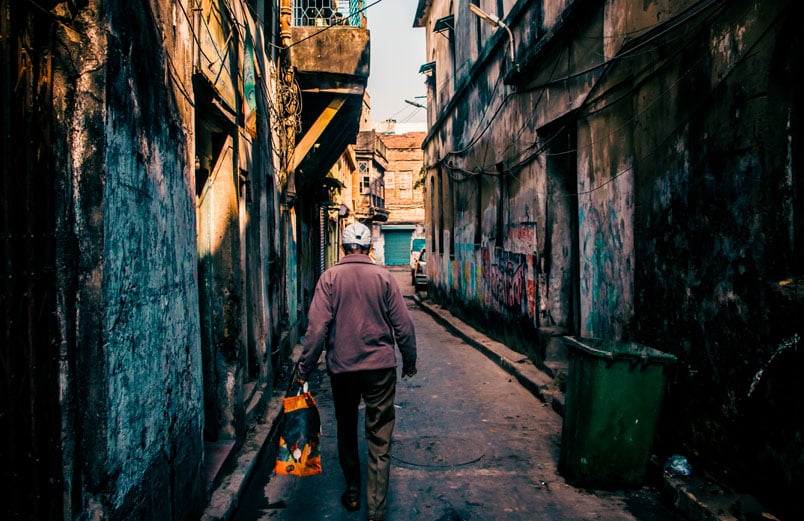 A man carrying a bag, walking down an alley in a city, away from the viewer.