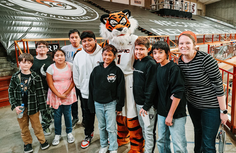 A university basketball game A woman with a group of children posing at with the University of the Pacific mascot, at a game.
