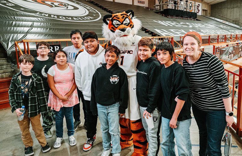 A woman with a group of children posing at with the University of the Pacific mascot, at a game.