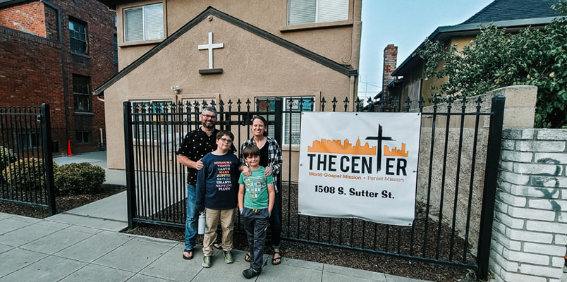 A husband and wife pose with their two sons in front of a building with a cross next to a sign that says The Center