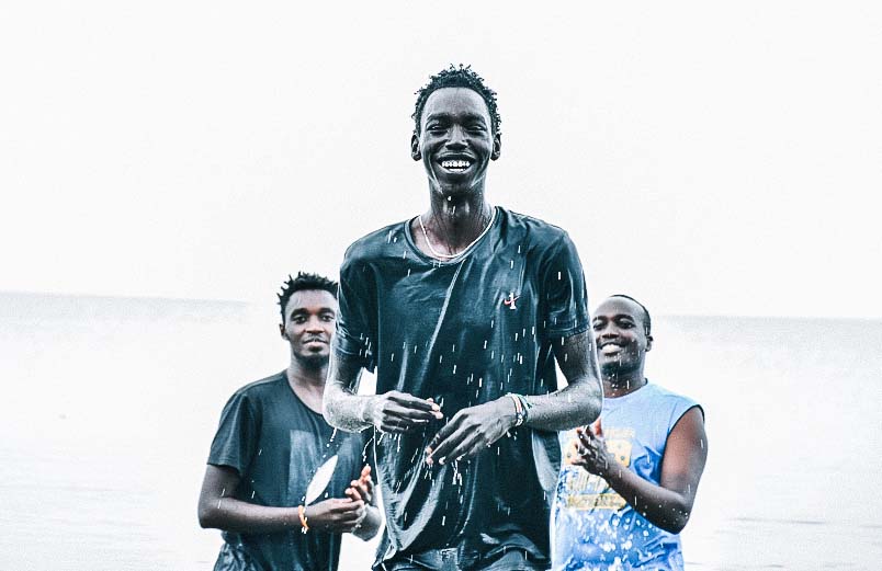 A joyful Eddie after his baptism A grinning young man walking towards shore with two men who baptized him standing in the background.