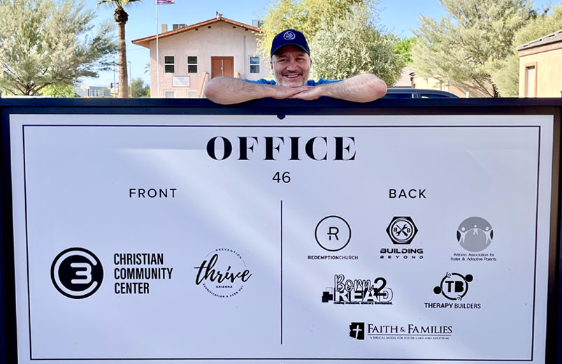 A smiling man stands behind a sign for a ministry center