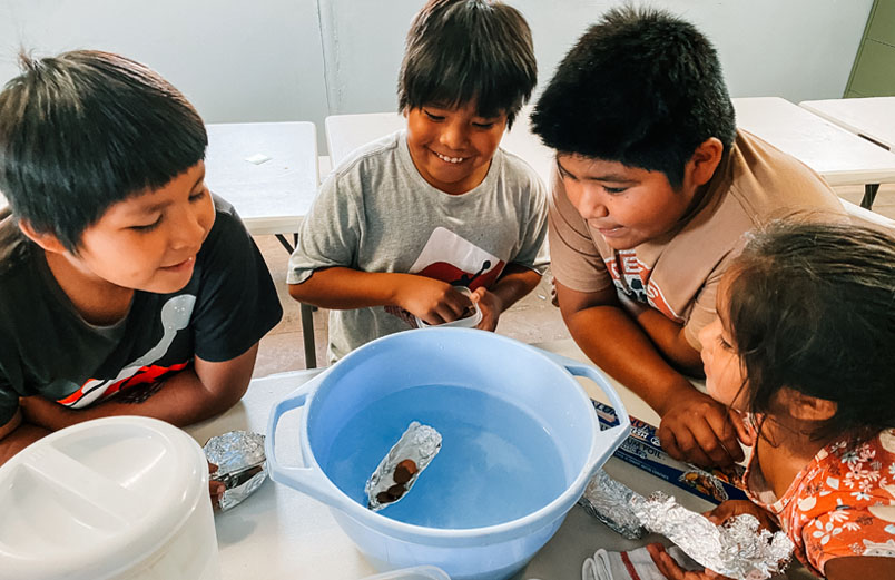 Four Native American children gather around a bowl full of water for an activity.