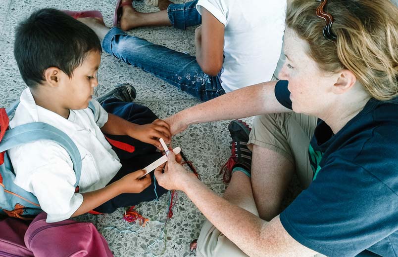 A woman helping a small child make a cross from popsicle sticks..