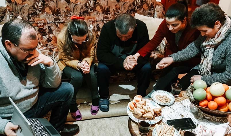 Those in the home, with their heads bowed and some holding hands, praying together with the team members on the Zoom call.