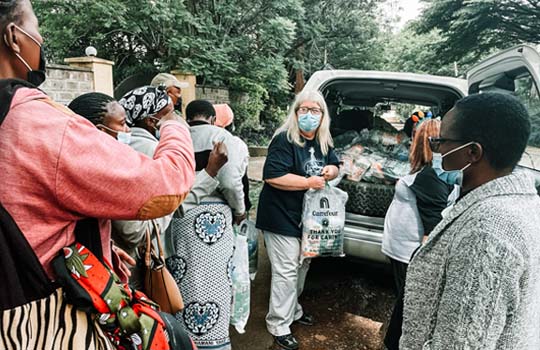 Three women handing out bags of food from the back of a car