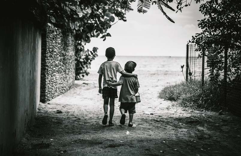 Two young boys walking down a path, the older one with his arm resting on the shoulders of the younger.