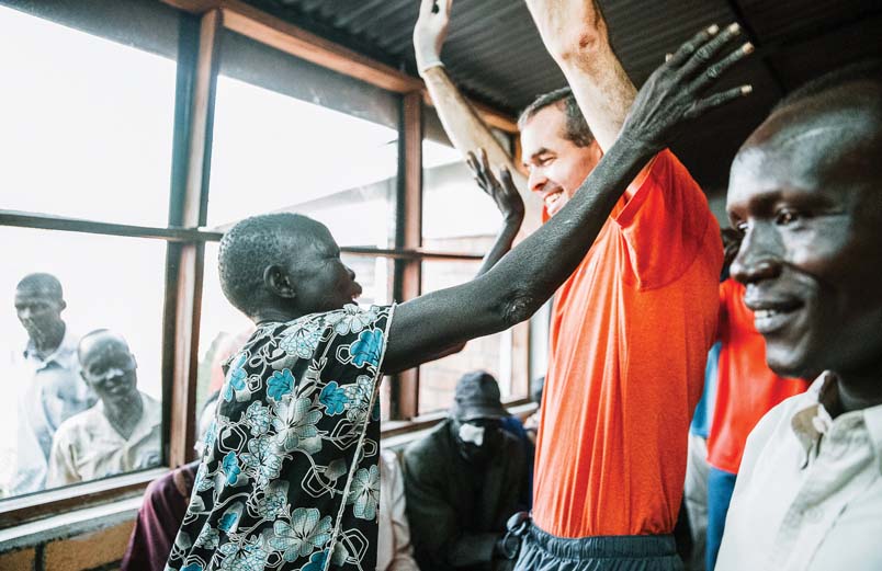 A patient with a big smile on her face facing the surgeon, both of their arms raised high as they rejoice that she can see again.