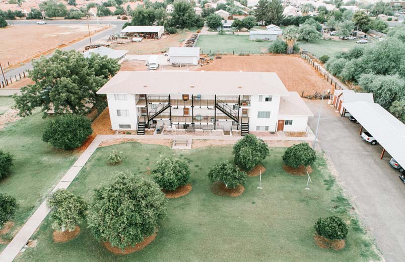 A three story apartment building with a lawn and trees and a parking shelter on the side