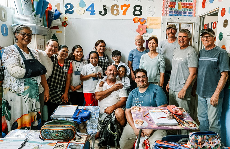 Fifteen smiling people, from elementary age to senior adults in a brightly decorated classroom